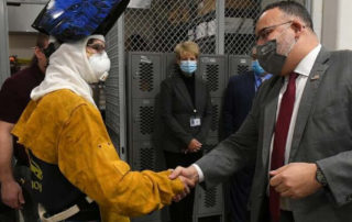 Ella T. Grasso Technical High School junior Tyler White, wearing a helmet and protective gear shaking hands with U.S. Secretary of Education Miguel Cardona