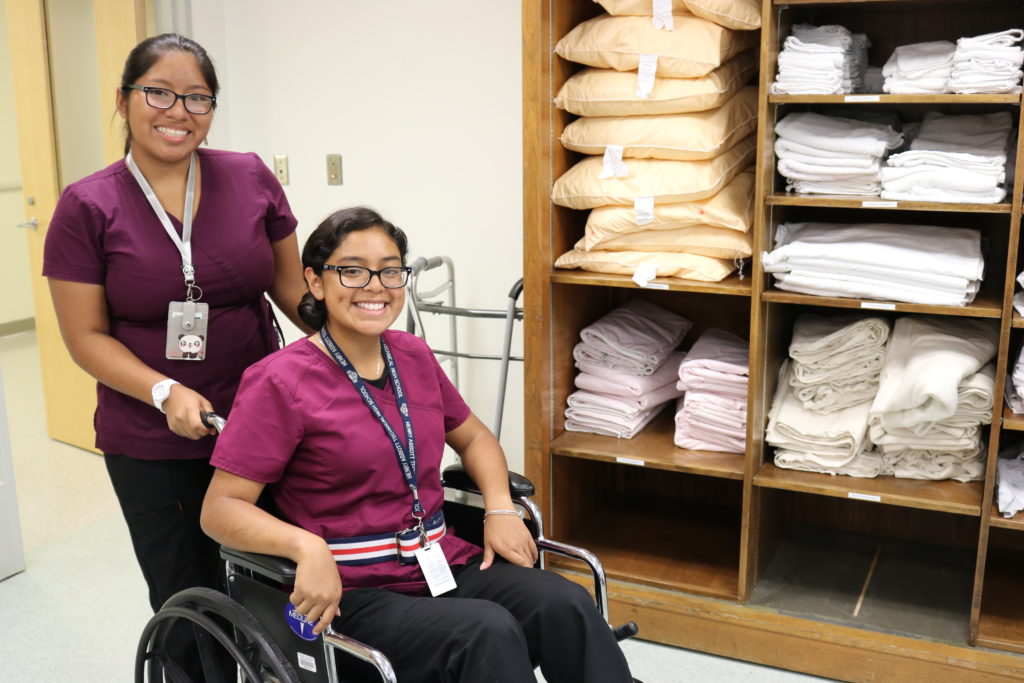 Health Technology students smile for the camera while practicing skills, one sits in a wheelchair