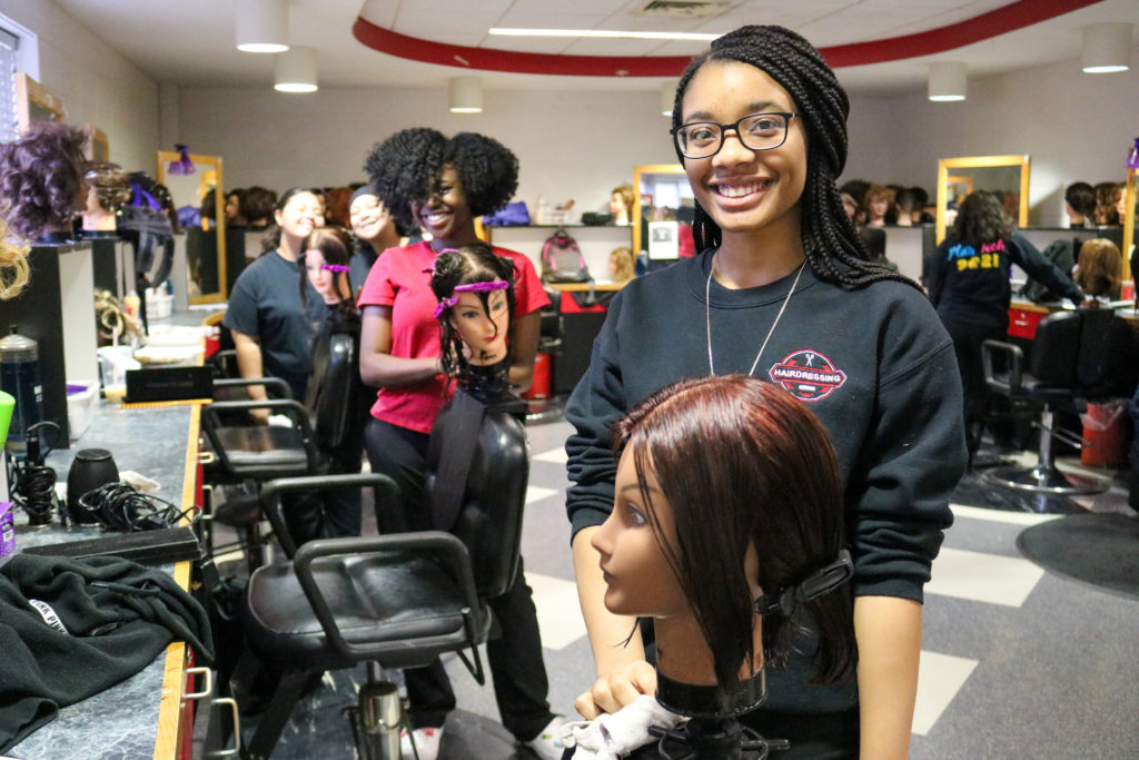 Hairdressing students smile with their practice mannequin heads while in the shop