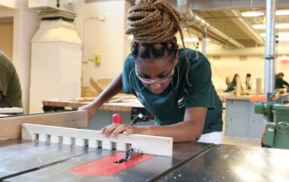 Carpentry student working in shop to cut a piece of wood for a project