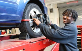 Automotive Technology student smiles for the camera as he works on a car in the shop