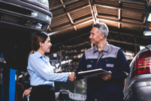 Young female car service manager giving quotation on a clipboard to senior male client and customer