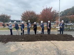 Dignitaries stand behind a pile of dirt holding shovels to signify the ground breaking of a new solar project