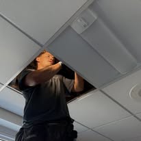 A worker stands on a ladder while installing a new LED fixture in the school hallway.