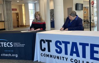 CTECS' Executive Director Dr. Alice Pritchard and CT State's President Royal sit at two tables and sign the agreement