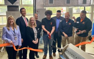 Representatives from CTECS, Shaffer Beacon Mechanical and Torrco, DCP Commissioner Bryan T. Cafferelli, DOL Deputy Commissioner Mark Polzella, and Tracy Ariel, OWS Director of Business Engagement cutting a ribbon with E.C. Goodwin HVAC students to celebrate an equipment donation.