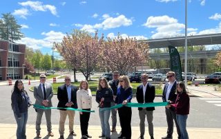 Students from Howell Cheney Technical High School cut the ribbon on the new carport solar energy system (in background), joined by Principal David Batch, DAS Commissioner Michelle Gilman, CTECS Executive Director Dr. Alice Pritchard, and project partners from the Connecticut Green Bank and Verogy.